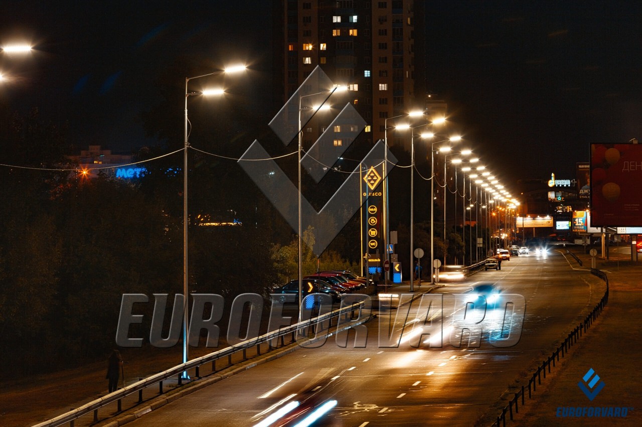 Опори вуличного освітлення біля дороги в темряві на фоні міських будівель