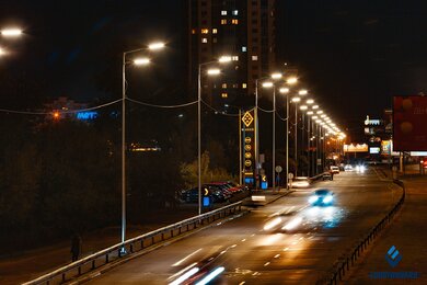 Опоры уличного освещения возле дороги в темноте на фоне городских построек