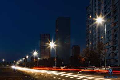 Опоры уличного освещения в городе, на фоне зданий и дороги в сумерках