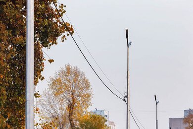 Опоры уличного освещения в городе на фоне пешеходной дорожки к застройке