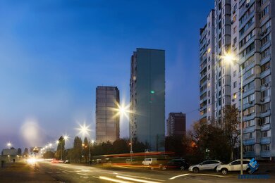 Опори вуличного освітлення в місті, на фоні дороги та будинків зліва