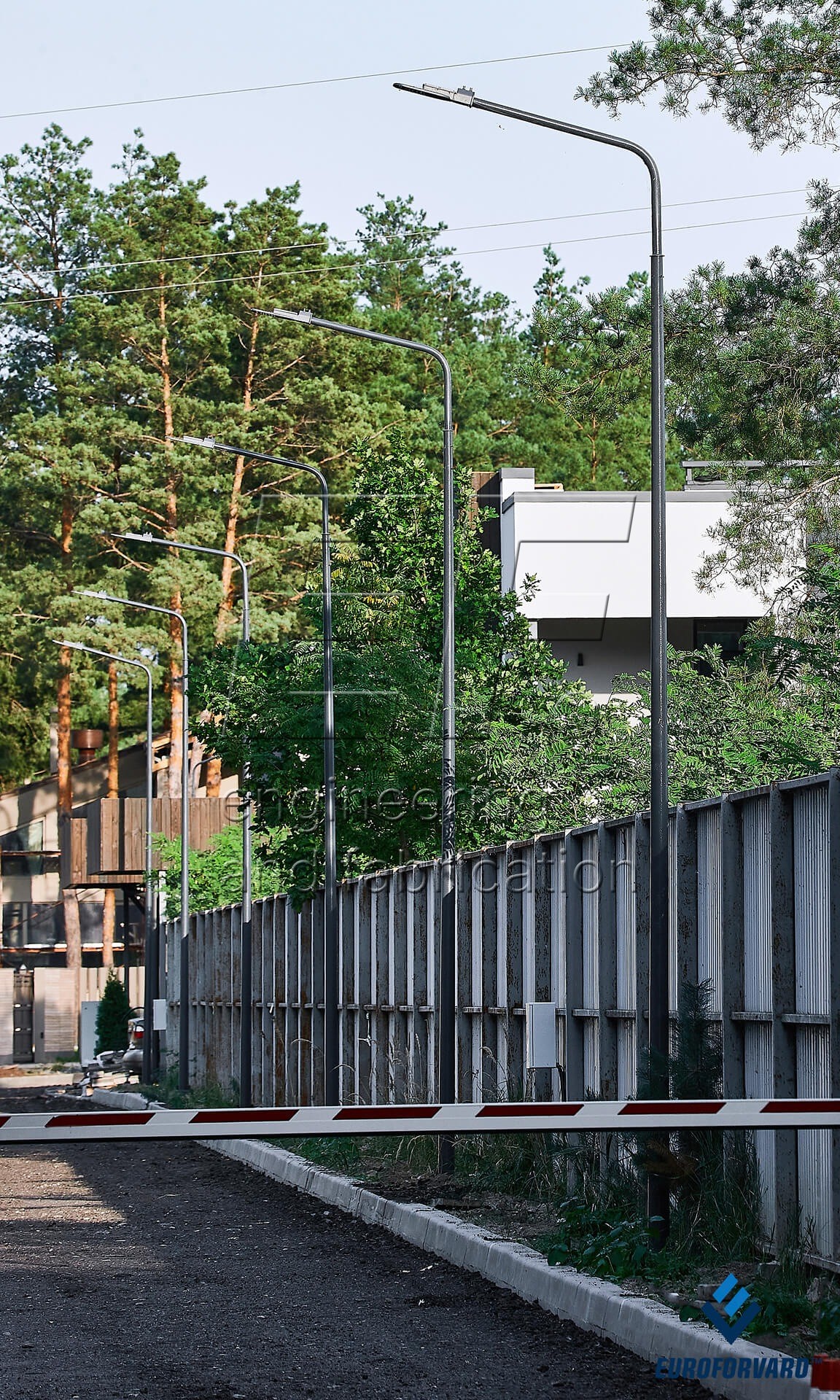 Опори паркового освітлення біля паркану на фоні дерев