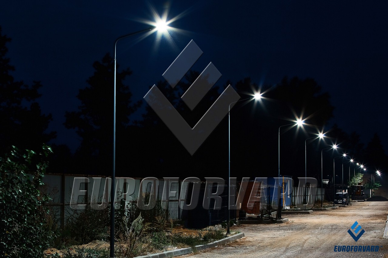 Опори паркового освітлення біля дороги та паркану вночі