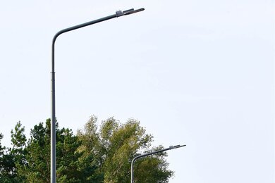 Опоры паркового освещения возле дороги на фоне деревьев