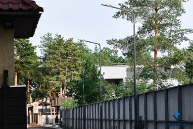 Опоры паркового освещения возле забора днем