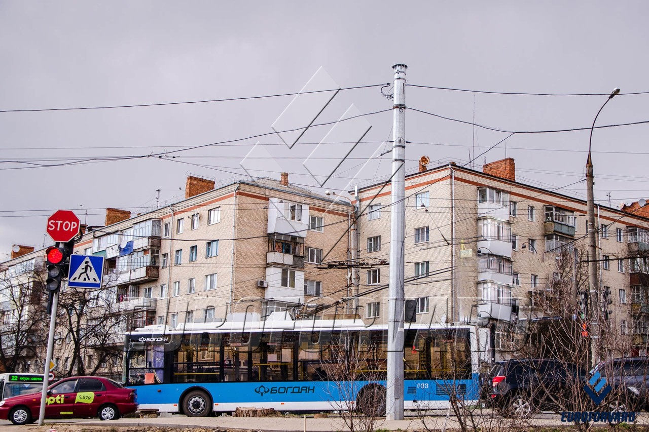 Опори контактної мережі біля дороги на фоні міських будівель