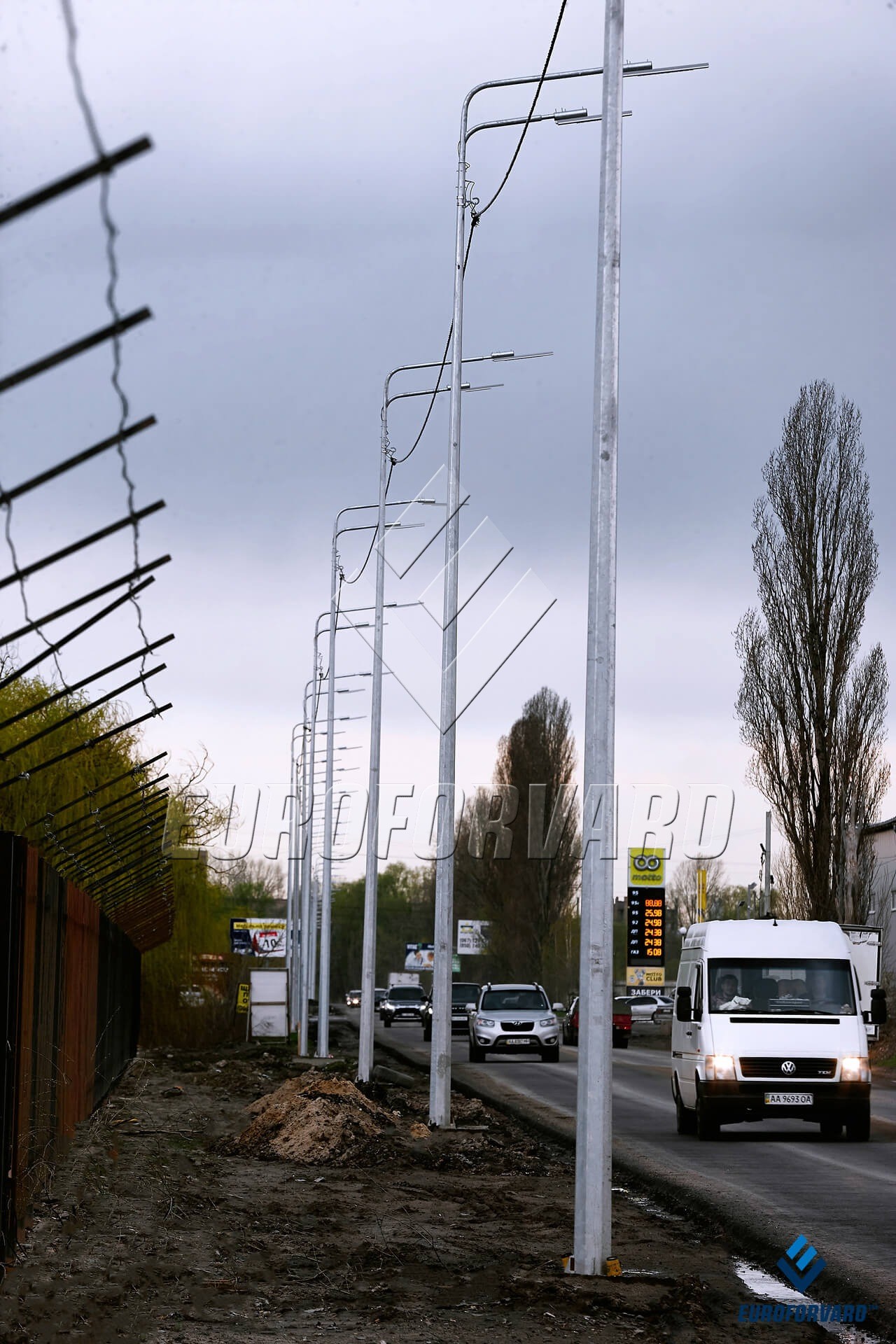 Опоры уличного освещения с двухрядными кронштейнами вдоль дороги днём
