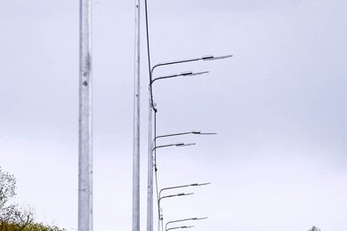 Опоры уличного освещения с двухрядными кронштейнами возле дороги днём