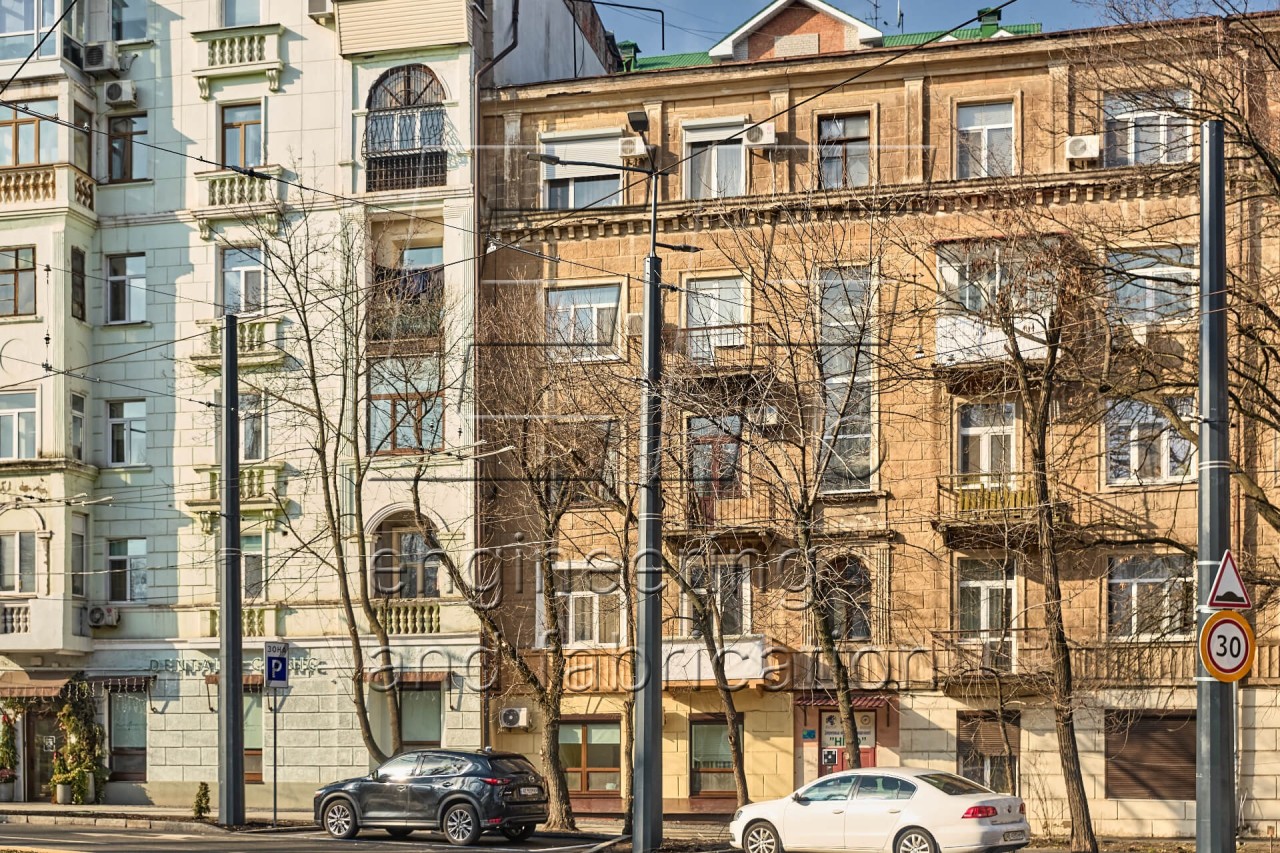 Опори контактної мережі багатогранні на фоні будівель міста